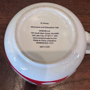 May include: White ceramic mug with a red and black design. The bottom of the mug features text including "&copy; Disney", "Microwave and Dishwasher Safe", and "NOT A TOY".