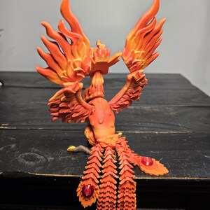 May include: A detailed orange and red phoenix figurine with outstretched wings and a flowing tail. The sculpture features intricate feather detailing and red jewel accents, creating a vibrant and dynamic display. The figurine is a decorative item.