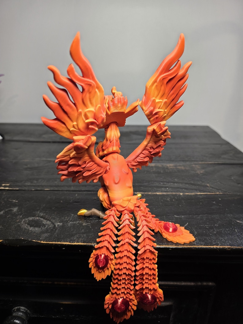 May include: A detailed orange and red phoenix figurine with outstretched wings and a flowing tail. The sculpture features intricate feather detailing and red jewel accents, creating a vibrant and dynamic display. The figurine is a decorative item.