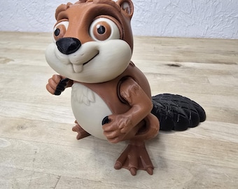 May include: A 3D-printed cartoon beaver figurine. The beaver has brown fur, a white belly, and a black tail. It has large, expressive eyes and is posed with its arms slightly raised. The figurine is sitting on a wooden surface.