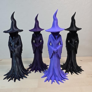 May include: Four standing figurines of robed figures wearing pointed hats, arranged in a row. Two are black, one is dark purple, and one is light purple. Each figure features long, flowing sleeves and a hem that flares out at the base like roots.