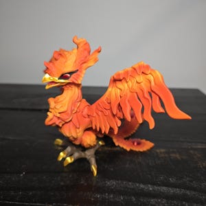 May include: A detailed figurine of a phoenix, predominantly orange with yellow and red accents. The mythical bird is perched on a branch, with its wings spread. The figurine has a detailed, textured appearance.