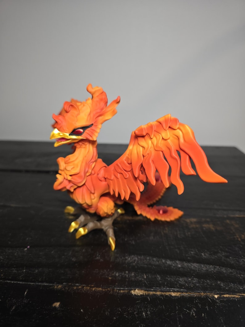 May include: A detailed figurine of a phoenix, predominantly orange with yellow and red accents. The mythical bird is perched on a branch, with its wings spread. The figurine has a detailed, textured appearance.