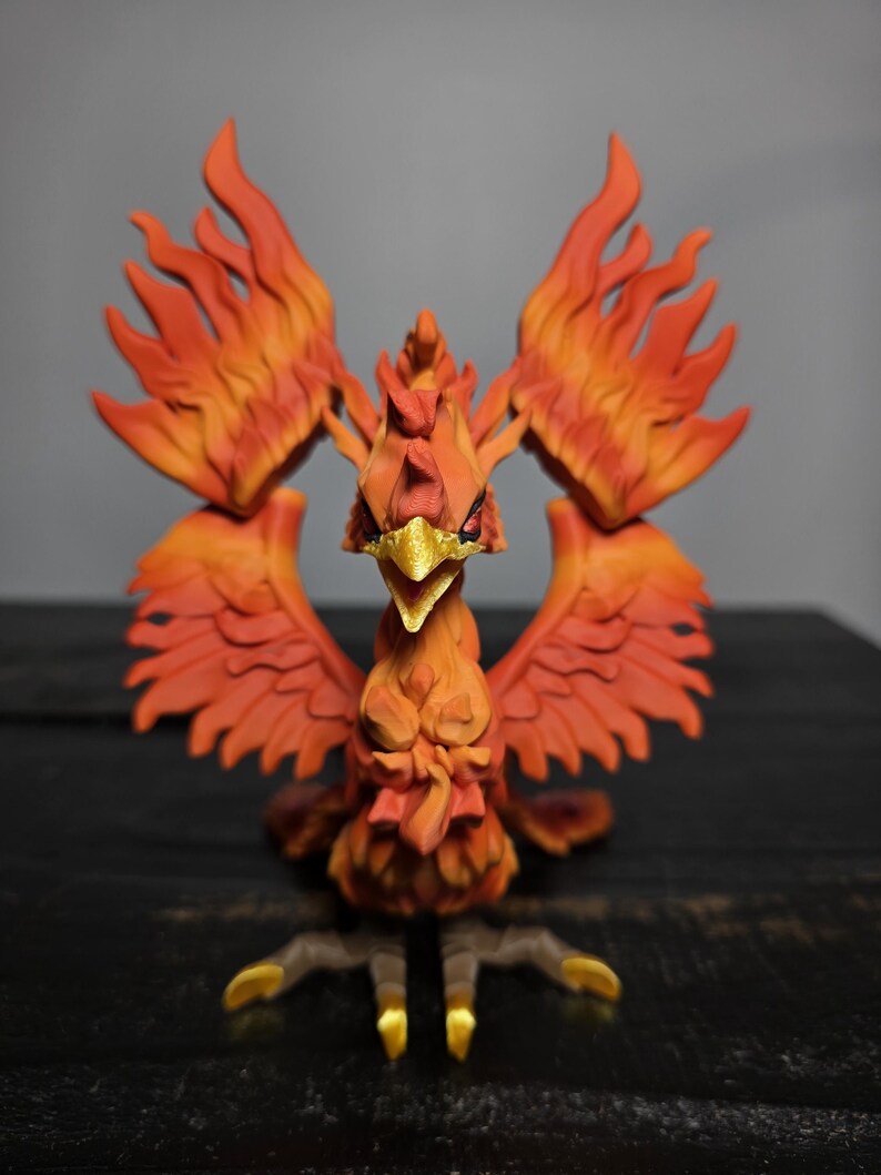 May include: A detailed, orange and red phoenix figurine with outstretched wings. The bird has a golden beak and talons, and its feathers are sculpted to resemble flames. The figurine is set against a dark background.