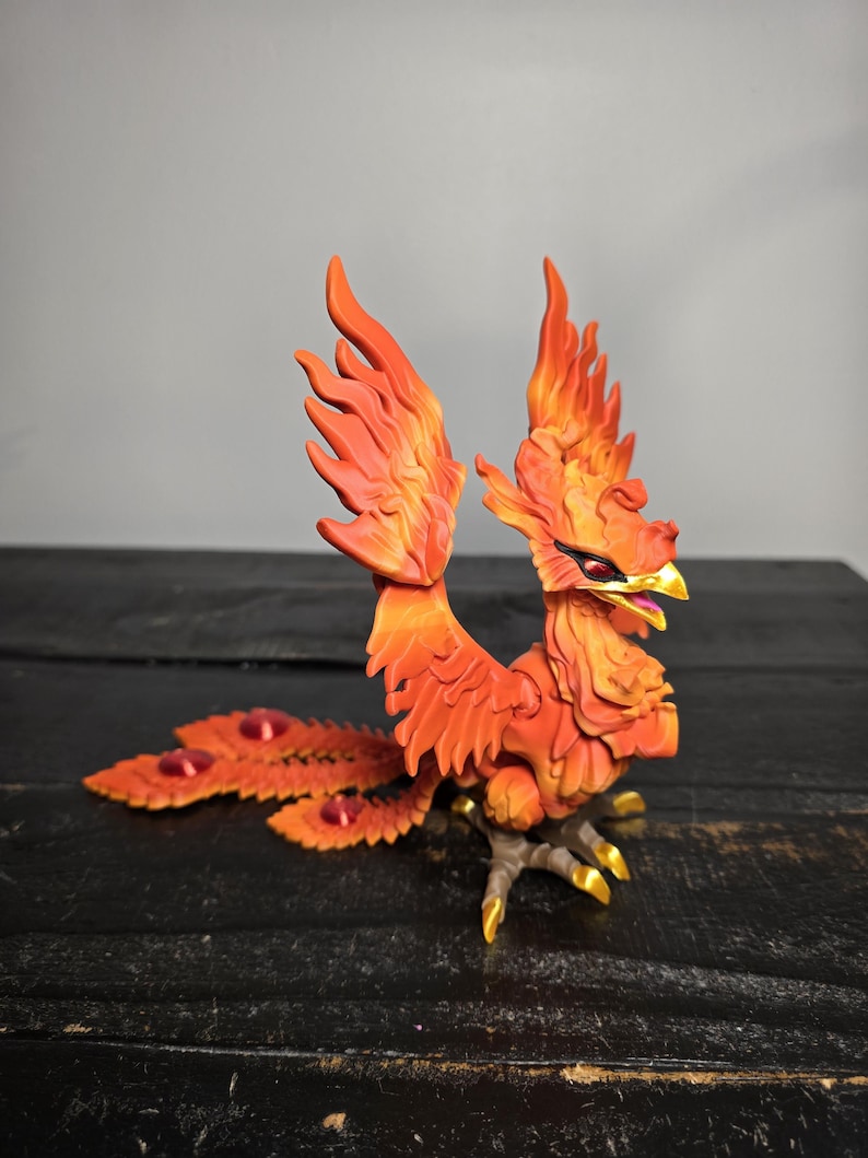 May include: A detailed figurine of a phoenix, featuring vibrant orange and red hues. The mythical bird has outstretched wings and a flowing tail with red accents. The phoenix stands on a dark surface, showcasing its golden talons and beak.