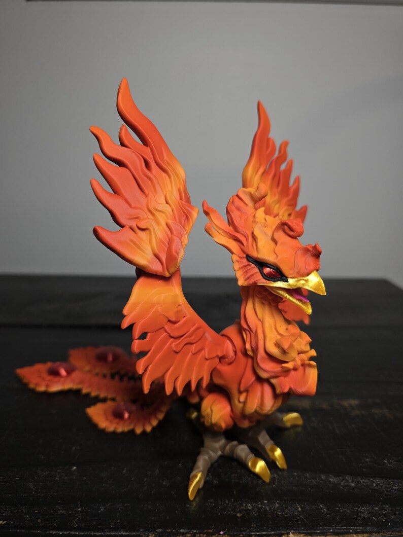 May include: A detailed figurine of a phoenix with fiery orange and yellow feathers. The mythical bird has a red eye, a golden beak, and golden talons. The wings are spread, and the tail features red accents.