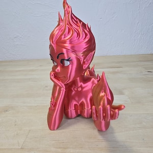 K&ouml;nnte beinhalten: 3D-gedruckte Figur eines weiblichen Charakters mit feuerrotem Haar und einer Flamme in der Hand. Die Figur posiert mit dem Kinn auf der Hand und ist in Rot- und Oranget&ouml;nen gehalten.