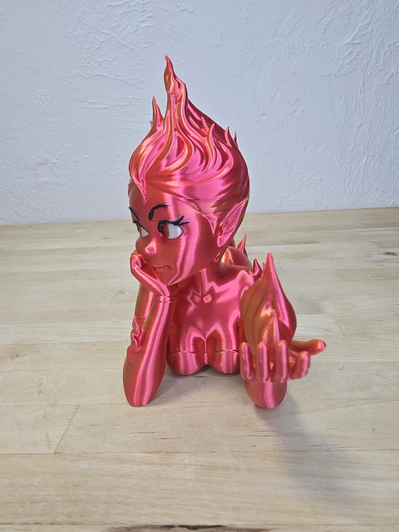 K&ouml;nnte beinhalten: 3D-gedruckte Figur eines weiblichen Charakters mit feuerrotem Haar und einer Flamme in der Hand. Die Figur posiert mit dem Kinn auf der Hand und ist in Rot- und Oranget&ouml;nen gehalten.