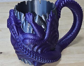 May include: A purple dragon-shaped mug with a silver interior. The dragon's head and tail form the handle of the mug.