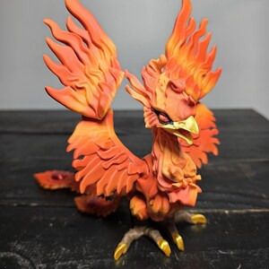 May include: A detailed figurine of a phoenix, featuring vibrant orange and yellow hues. The bird's wings are spread, showcasing intricate feather details. The beak and talons are accented with gold, creating a striking contrast.