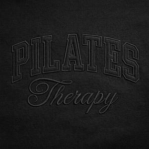 Puede incluir: Tela negra con el texto bordado "PILATES Therapy". La palabra "PILATES" está arqueada sobre la palabra "Therapy" en una fuente de estilo script. El texto está en una fuente de estilo universitario. El fondo es de color negro sólido.