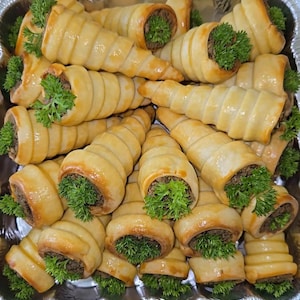 May include: A platter of small, golden brown pastry cones filled with a savory meat mixture and topped with fresh parsley.