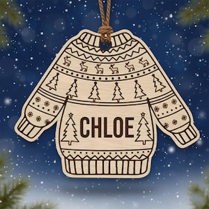 以下が含まれることがあります： 「CHLOE」という名前が中央に書かれた、セーターの形をした木製のクリスマスオーナメント。セーターのデザインには、トナカイ、クリスマスツリー、雪の結晶の模様が含まれています。吊り下げ用の茶色の紐が付いています。