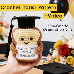 Pode incluir: Uma figura de torrada de crochê feita à mão usando um chapéu de formatura e óculos, segurando uma placa que diz "A Little Toast to Your Graduation". A imagem inclui o texto "Crochet Toast Pattern + Video" e "Handmade Graduation Gift".