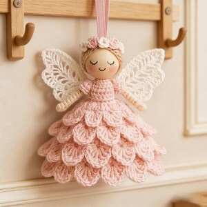 Peut inclure: Ornement en forme d'ange en crochet rose fait &agrave; la main, avec des ailes en dentelle blanche et une couronne florale. La t&ecirc;te de l'ange est en bois avec des traits peints, suspendu par un ruban rose. Un objet d&eacute;coratif charmant.