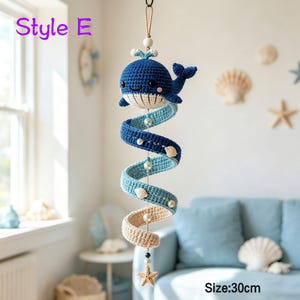 May include: A hanging crochet mobile featuring a dark blue whale with a cream-colored belly, suspended above a spiral tail that transitions from dark blue to light blue and cream. The mobile includes white beads and small seashells, measuring 30cm.
