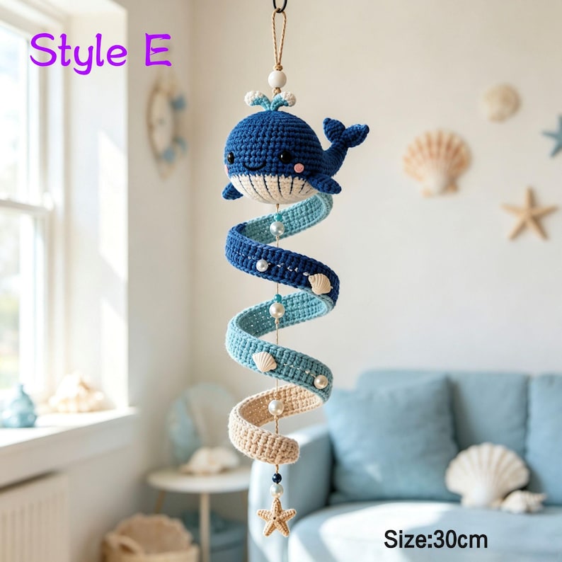 May include: A hanging crochet mobile featuring a dark blue whale with a cream-colored belly, suspended above a spiral tail that transitions from dark blue to light blue and cream. The mobile includes white beads and small seashells, measuring 30cm.