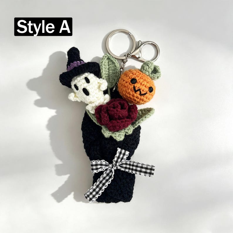 May include: A crochet keychain labeled Style A featuring a white ghost wearing a purple-trimmed black hat, an orange pumpkin with a green stem, and a dark red rose. The items are bundled in a black crochet wrap tied with a black and white gingham ribbon.