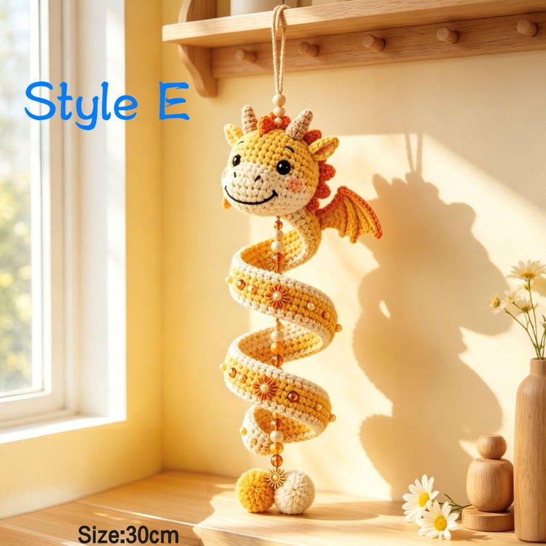 K&ouml;nnte beinhalten: Ein h&auml;ngendes H&auml;kel-Drachenornament in Gelb und Creme mit orangefarbenen Akzenten, einem spiralf&ouml;rmigen K&ouml;rper, kleinen Fl&uuml;geln und einer zentralen Perlenschnur. Der Text 'Style E' und 'Size:30cm' ist sichtbar. Der Drache hat ein l&auml;chelndes Gesicht.