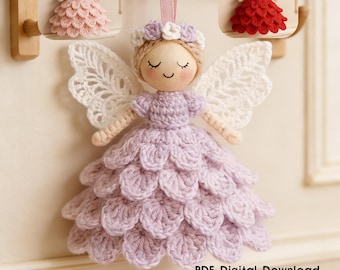 May include: A handmade crochet angel with a lavender dress, white lace wings, and a wooden head. The angel has a floral crown and is hanging from a pink ribbon. Two smaller angels in pink and red are also visible.