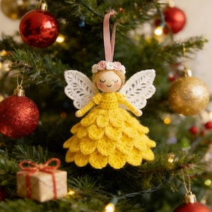 Peut inclure: Ornement de No&euml;l fait &agrave; la main en forme d'ange. L'ange a une t&ecirc;te en bois, une robe jaune crochet&eacute;e et des ailes en dentelle blanche. Il est orn&eacute; d'une couronne florale et suspendu par un ruban rose.