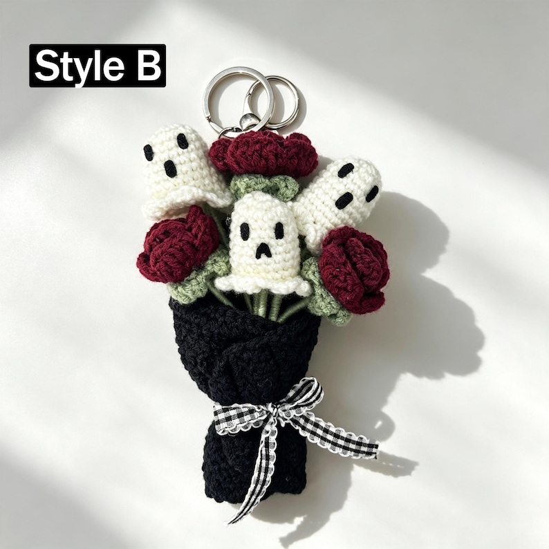 May include: A crochet keychain featuring a bouquet of three white ghost figures with black embroidered faces and three dark red roses with green stems, all wrapped in black yarn with a black and white gingham ribbon and a metal ring. Text: Style B.