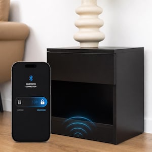 May include: A black bedside table with a drawer and open shelf, next to a smartphone showing a Bluetooth connection interface. The phone displays a lock icon and the word "UNLOCKED". A vase with flowers sits on top.