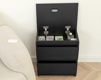 May include: A black three-drawer bedside cabinet with a hinged top lid that opens to reveal a storage compartment containing various paper currency and a small glass bottle. The unit features metal hinges and a smooth matte finish.