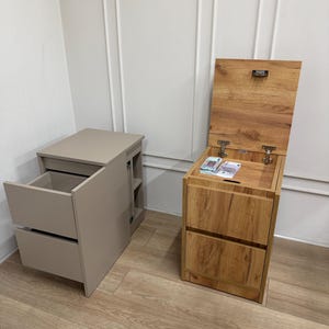 Pode incluir: Duas mesinhas de cabeceira de madeira. Uma é de cor castanho claro com duas gavetas e uma gaveta retrátil. A outra é de cor castanho mais escuro com uma tampa elevatória e duas gavetas. As mesinhas de cabeceira estão num canto de uma divisão com paredes claras.