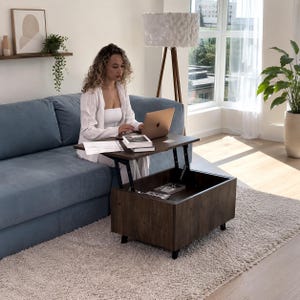 May include: A dark brown wooden coffee table with a lift-top mechanism that elevates the surface to desk height. The table features a rectangular base with internal storage space visible beneath the raised top, supported by black metal hinges.