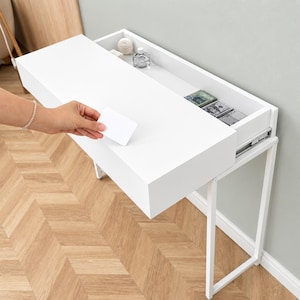 May include: A white floating console table with a single pull-out drawer featuring a smooth matte finish. The drawer is partially open, revealing a shallow interior compartment containing small glass bottles and stacks of paper currency.