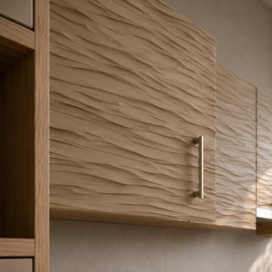 May include: A light brown wooden cabinet door featuring a textured, wavy, horizontal relief pattern across its surface. The cabinet door is equipped with a single, vertical, cylindrical metal handle in a brushed silver finish.