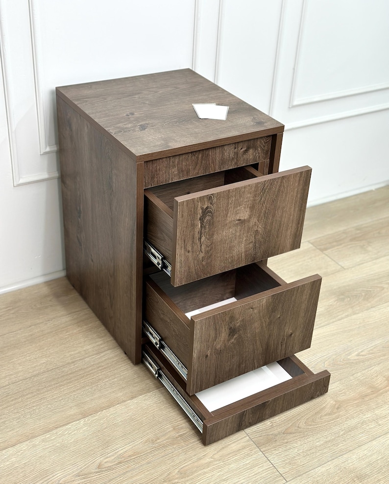 May include: A dark brown wood-grain finish filing cabinet featuring three stacked drawers with metal sliding tracks. The top surface is flat and rectangular, and the drawers are shown in an open position, revealing the interior structure.