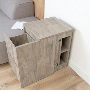 May include: A light brown wood-grain side table featuring a rectangular top, a pull-out storage compartment with a deep interior, and two open side shelves. The unit includes visible metal drawer slides on the side of the main storage section.