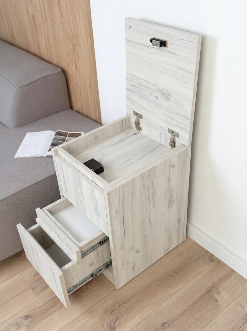 May include: A light wood grain bedside table with a vertical lift-top compartment featuring a metal latch and two pull-out drawers with metal sliding tracks. The unit has a rectangular frame and a light beige finish with visible wood grain patterns.