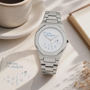 Könnte beinhalten: Eine silberfarbene Armbanduhr mit einem Gliederarmband aus gebürstetem Metall und einer achteckigen Lünette. Das weiße Zifferblatt zeigt den blauen Schriftzug 'Who cares I'm already late', verstreute blaue Zahlen und ein Datumsfenster mit der 25.
