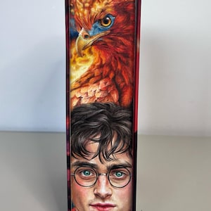 Può includere: Dorso di libro con un'illustrazione dettagliata di una fenice dai colori vivaci e un ritratto di un giovane con gli occhiali. La fenice è rossa, arancione e gialla. L'uomo ha i capelli scuri e gli occhi verdi.