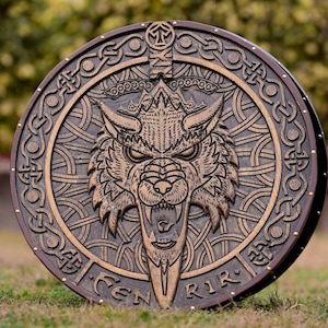 May include: A round wooden shield with a carved wolf head and a sword in the center. The shield is decorated with intricate Celtic knotwork and has a brown leather border.