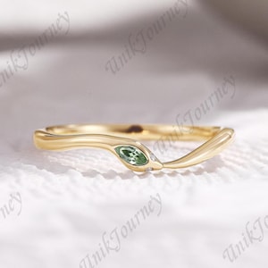 May include: A gold ring featuring a curved, snake-like band design. The head of the snake is set with a marquise-cut green gemstone and two tiny clear accent stones. The metal has a polished finish, and the band follows a gentle wave shape.