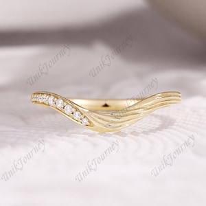 May include: A gold chevron-shaped ring featuring a row of small round clear stones set along one side and a textured, rippled surface pattern on the other side. The band has a curved, V-shaped design with a polished finish and the text UnikJourney.