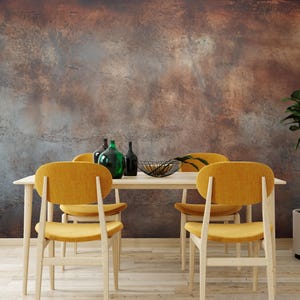 Könnte beinhalten: Ein Esszimmer mit einem hellen Holztisch und vier senfgelben Stühlen. Dekorative Glasflaschen und eine Drahtschale mit Obst stehen auf dem Tisch. Eine Topfpflanze befindet sich auf der rechten Seite, und die Wand hat ein strukturiertes, rostiges Aussehen.