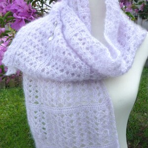 May include: A delicate, light purple crochet scarf with a lacy pattern. The scarf is draped over a white mannequin and is made of a soft, airy yarn.