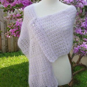 May include: A delicate, lacy shawl in a pale lavender colour, draped over a white mannequin. The shawl is made of a soft, lightweight yarn and has a delicate, openwork design.