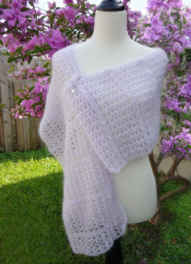 May include: A delicate, lacy shawl in a pale lavender colour, draped over a white mannequin. The shawl is made of a soft, lightweight yarn and has a delicate, openwork design.