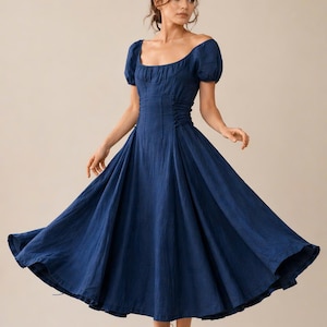 May include: A dark blue midi dress featuring a square neckline, short puff sleeves, and a fitted bodice with side ruching details. The skirt is full and flared, creating a wide silhouette that extends below the knees, crafted from a textured fabric.