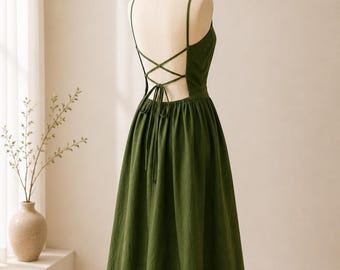 Op de afbeelding: Een donker olijfgroene midi-jurk met een diepe rug, voorzien van dunne, gekruiste bandjes die in de taille worden gestrikt. Het kledingstuk heeft een aansluitend lijfje, een uitlopende rok en dunne schouderbandjes, getoond op een paspop.