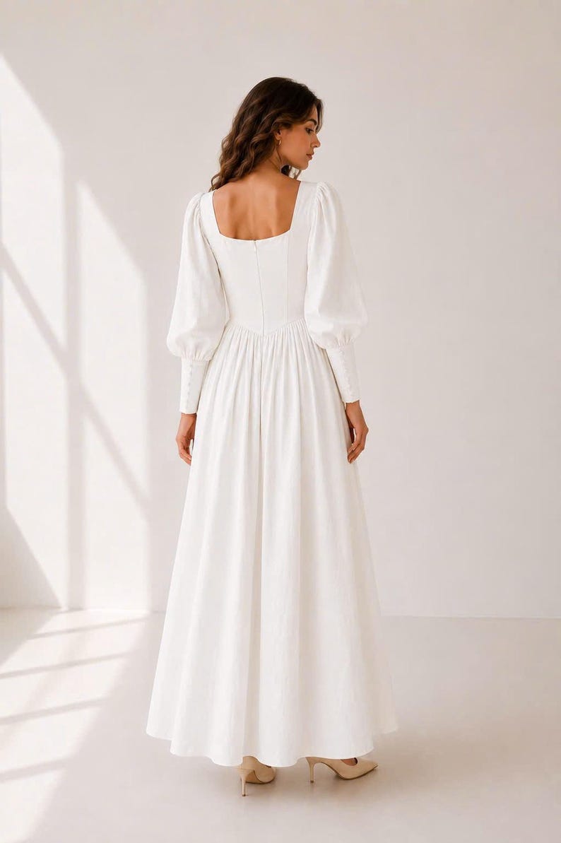 A woman wearing a long white dress with puffy sleeves stands facing away from the camera.