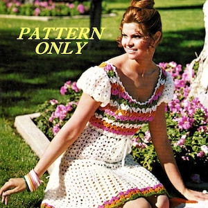 May include: A crochet dress pattern with a white base and colorful stripes of pink, orange, and green. The dress has a scoop neck and short sleeves. The model is wearing the dress and sitting on a colorful blanket.
