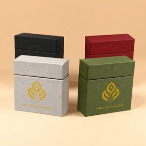 Peut inclure: Quatre boîtes rectangulaires noires, rouges, vertes et grises. Les boîtes grises et vertes ont un logo doré et le texte "EHIMARI Packaging". Les boîtes sont fermées et ont une surface texturée.