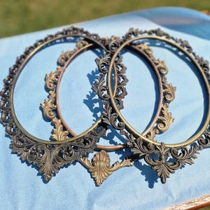 Peut inclure: Trois cadres photo de forme ovale ornés de volutes métalliques complexes et de détails en forme de feuilles. Les cadres présentent une finition bronze vieilli foncé avec des reflets dorés plus clairs sur les bords décoratifs en relief.